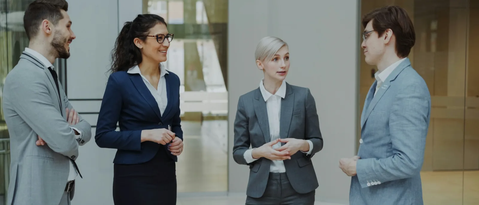 Four business professionals in conversation in a modern office lobby.